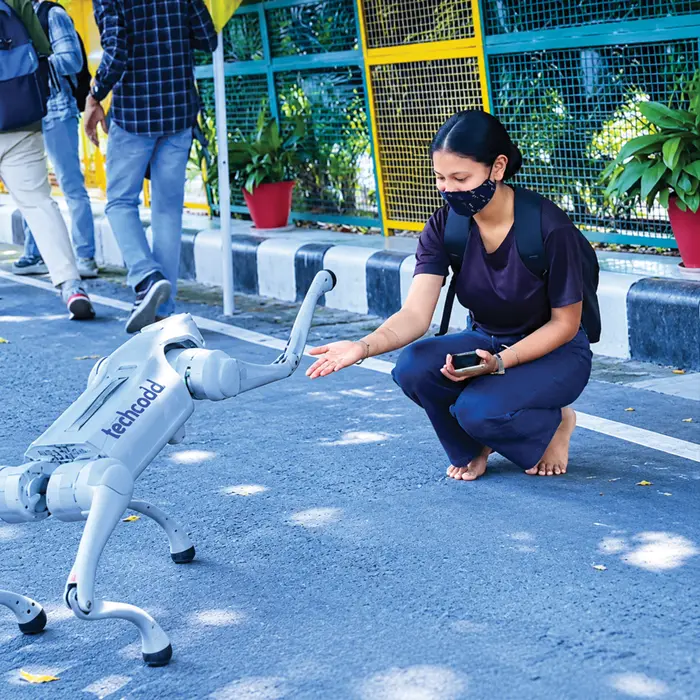 A student greeting the techcadd robot dog outside the campus