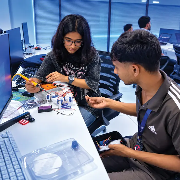 Two students soldering a small robot together in the lab