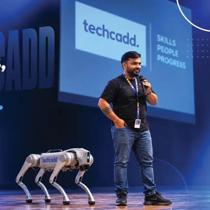 On stage at a techcadd event, the robot dog alongside the speaker