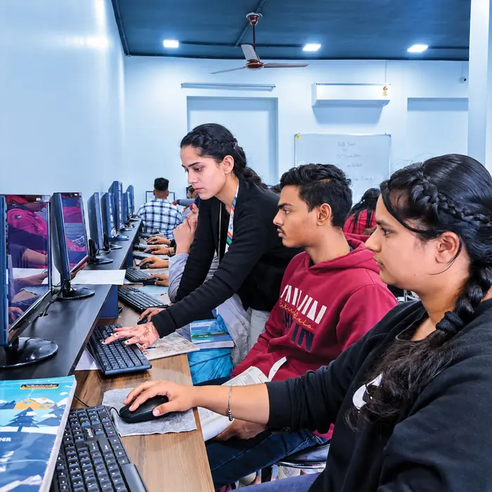 A trainer guiding students through an exercise at their desktops